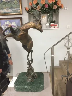Бронзовая антилопа в прыжке на каменистом постаменте и зелёной мраморной подставке, в интерьере с лестницей